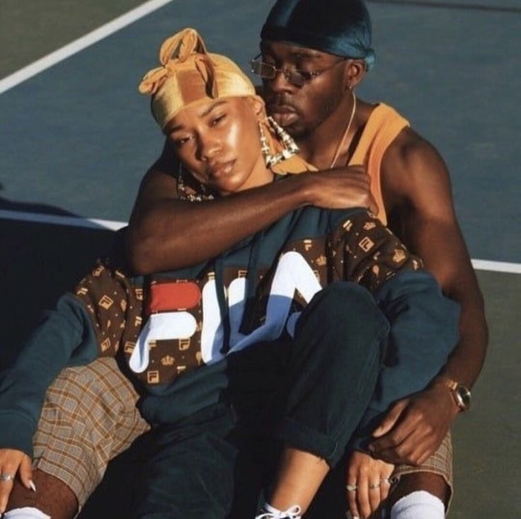 a man and woman sitting on top of a tennis court holding their arms around each other