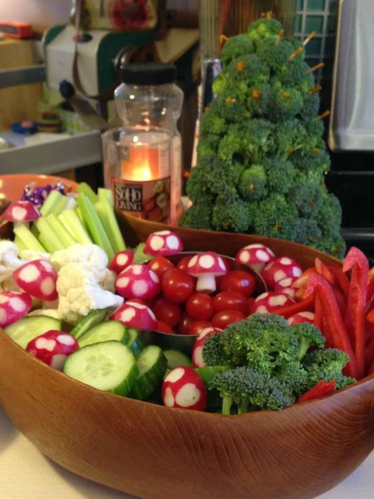 a wooden bowl filled with lots of veggies next to a lit candle on top of a counter