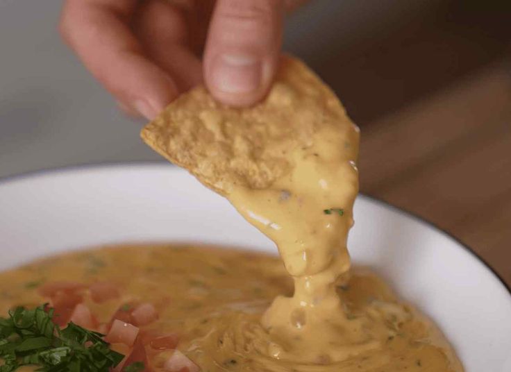 a person dipping tortilla chips into a bowl of soup