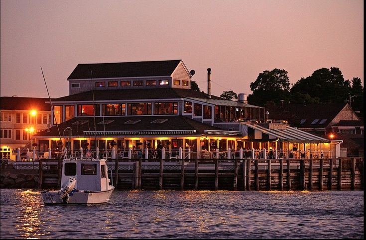 a boat is in the water at night near a restaurant with lights on it's roof