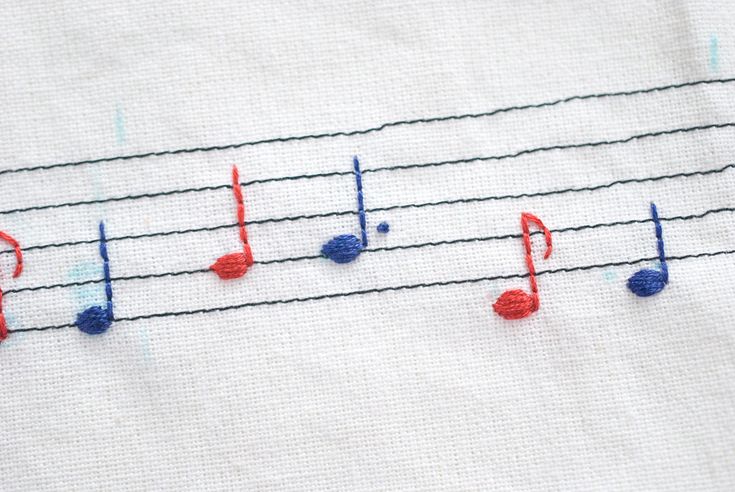 an embroidered sheet with musical notes and red, white, and blue thread on it