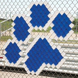 a blue and white quilt hanging on a chain link fence next to a parking lot