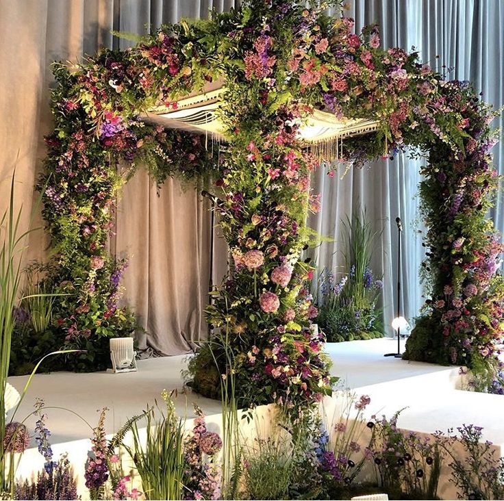 an outdoor wedding setup with flowers and greenery on the wall, along with drapes