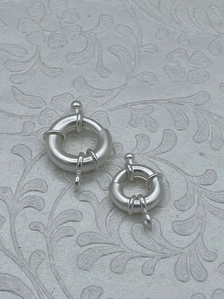 two pairs of silver colored metal hoop earrings on a white background with floral design pattern