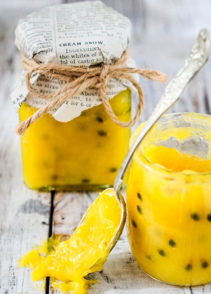 two jars filled with yellow pudding sitting on top of a wooden table next to a spoon