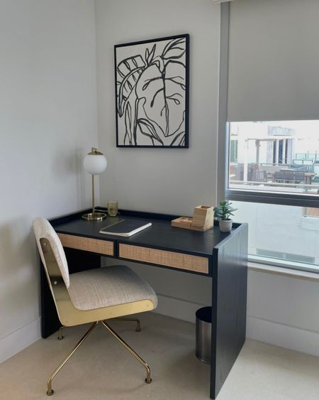 a desk with a chair next to it in front of a large window and a painting on the wall