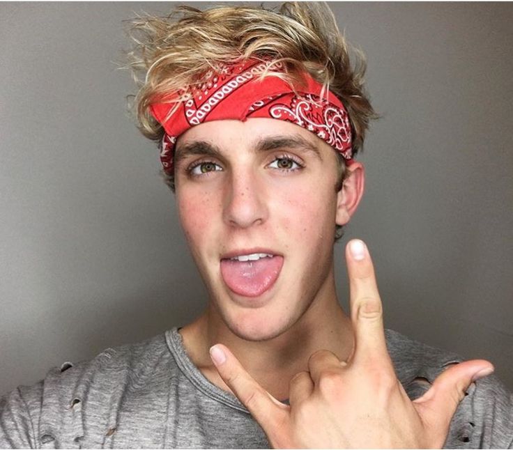 a young man wearing a bandana making the peace sign with his hand while standing in front of a gray wall