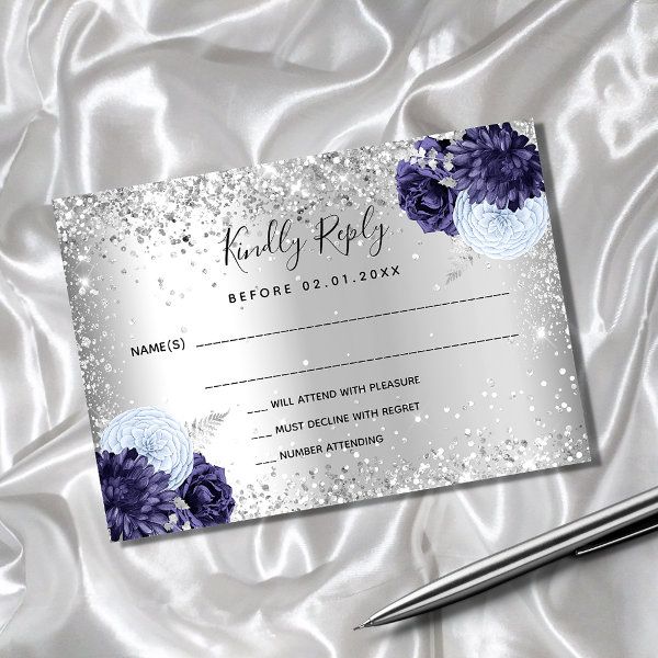 a silver and purple wedding response card with blue flowers on it, next to a pen