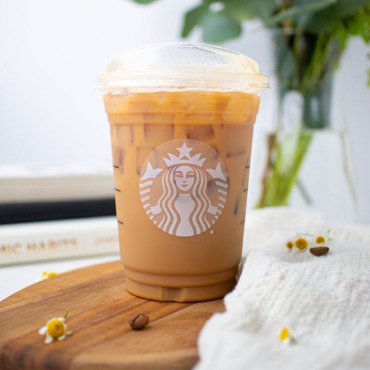 a cup of iced coffee sitting on top of a wooden table next to a plant