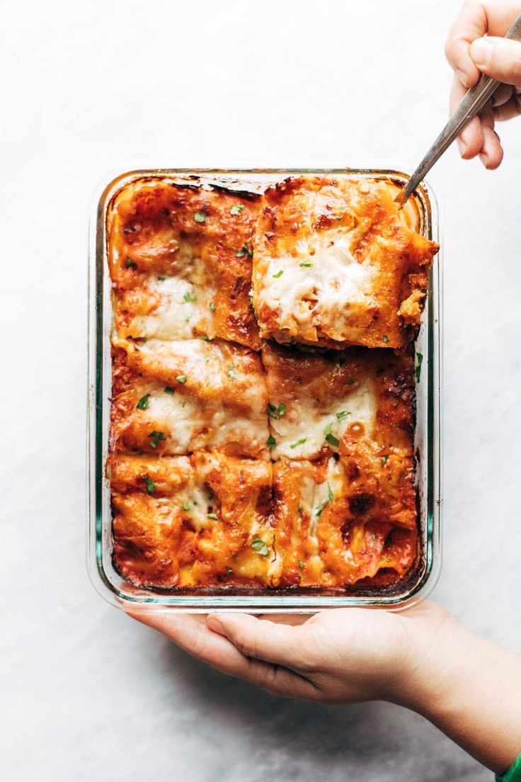 a person holding a spoon in a casserole dish with meat and cheese on it