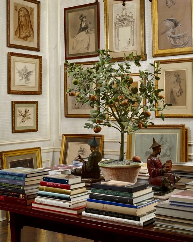 a table topped with lots of books next to pictures and a tree in a vase