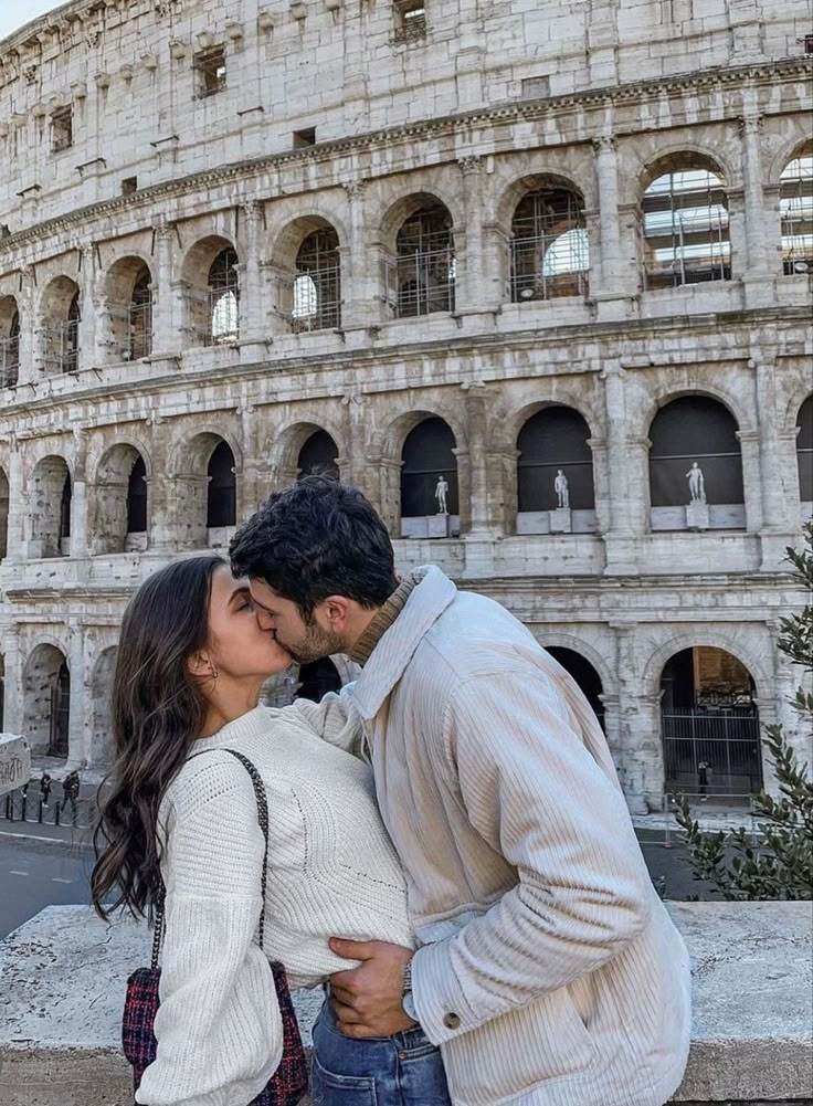 a man and woman kissing in front of the colossion