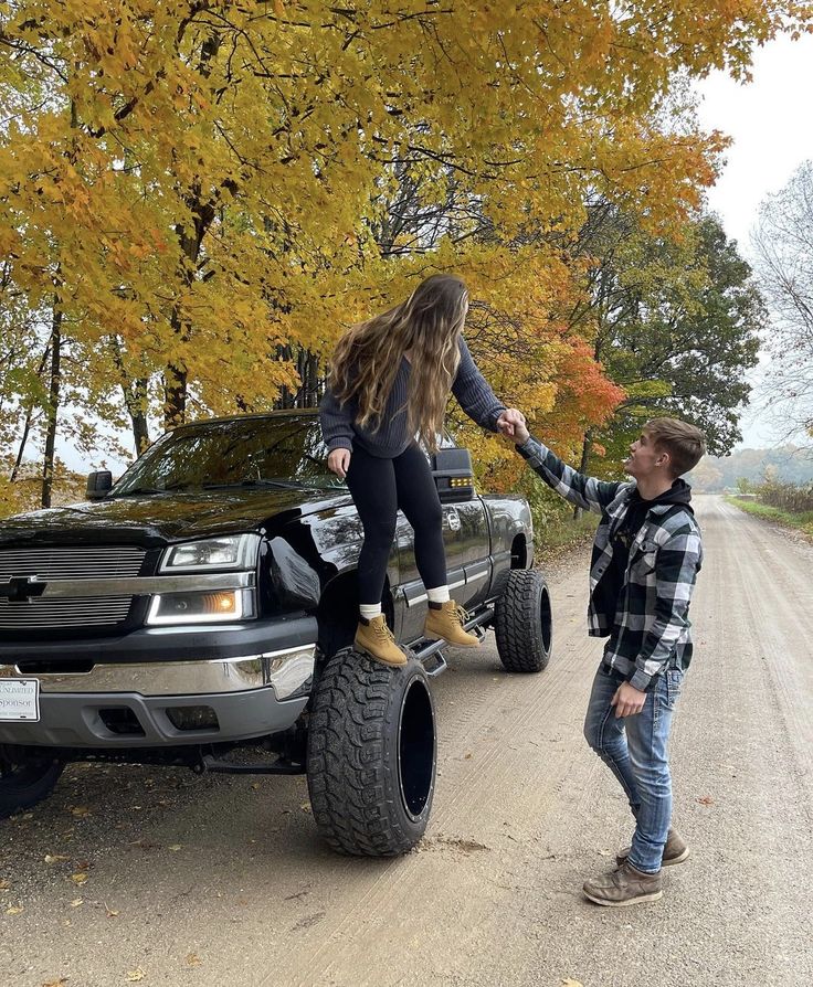 a woman standing on the back of a black truck while holding onto a man's hand