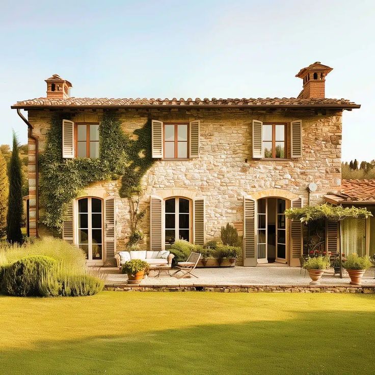 a large stone house with lots of windows and plants on the front lawn, surrounded by greenery