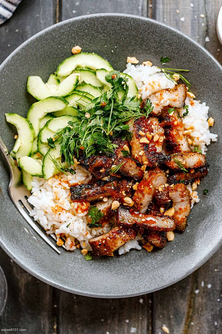 a bowl filled with rice and meat next to cucumbers on top of a wooden table