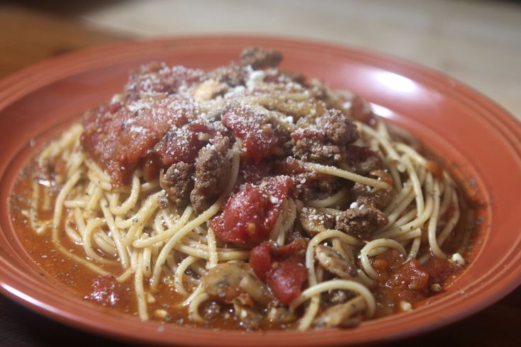 spaghetti with meat and tomato sauce on an orange plate sitting on a wooden table top