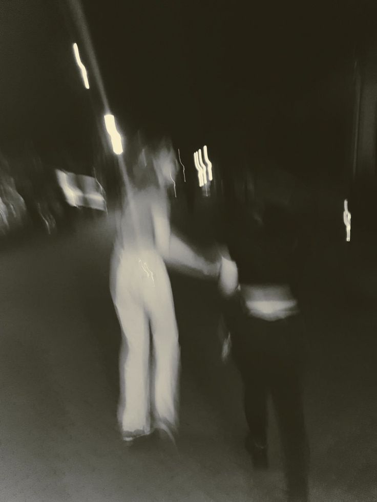 blurry photograph of two people walking down the street at night time, with one person holding another's hand