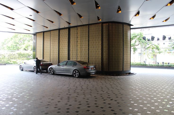 two cars parked next to each other in front of a tall building with gold and black panels