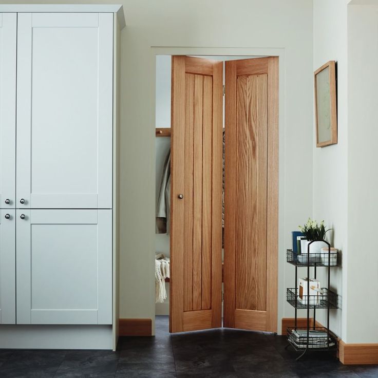 an open wooden door in a white room with black flooring and cabinets on either side