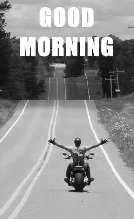 a man riding on the back of a motorcycle down a road with his arms outstretched