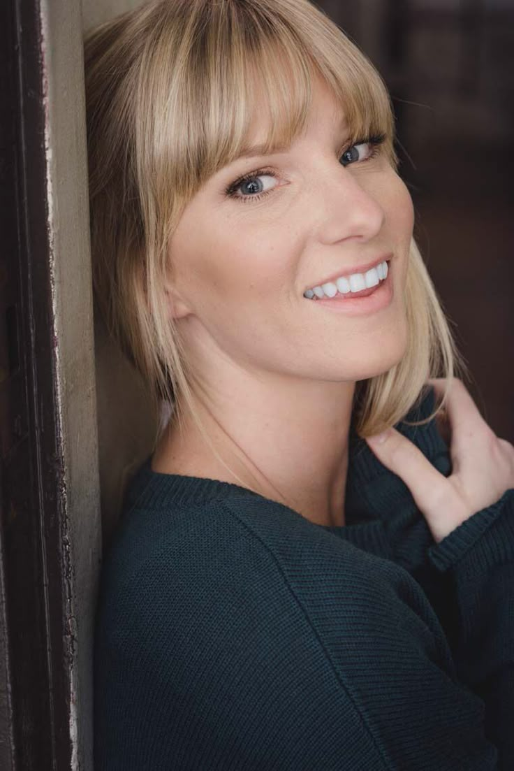 a woman with blonde hair smiling and leaning against a wall