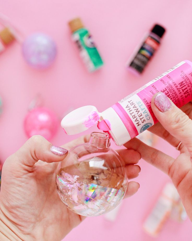 a woman is holding a small glass ball with pink liquid in it and some other items on the wall behind her