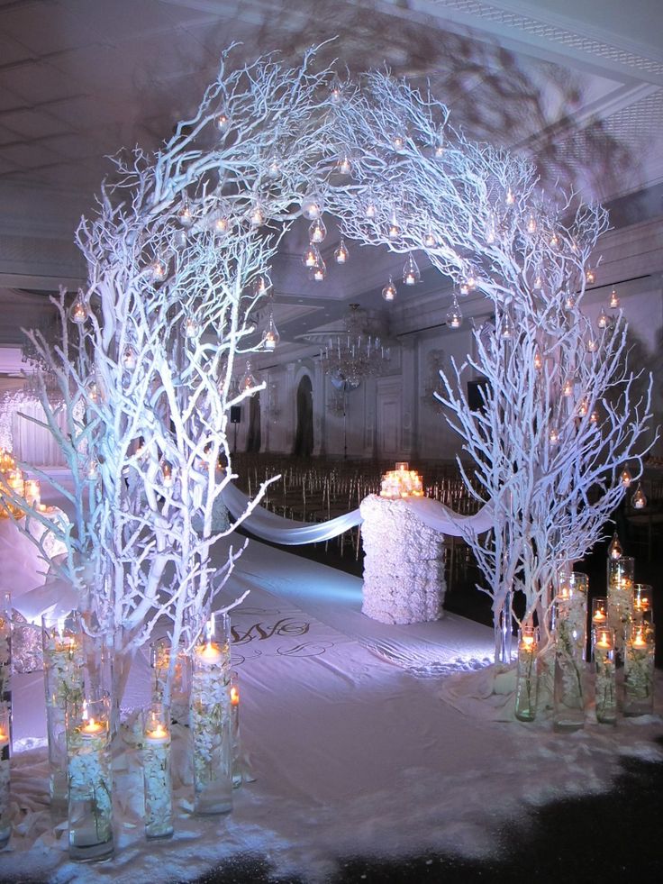 an archway decorated with white branches and candles for a winter wonderland wedding ceremony in the snow