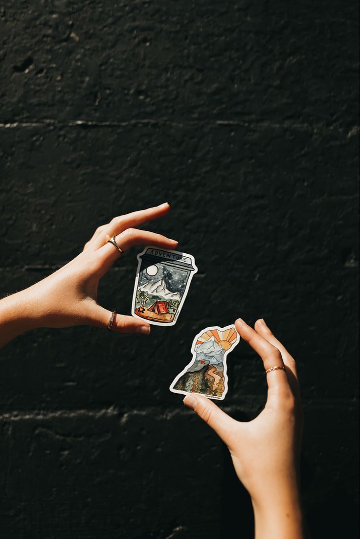 two hands holding playing cards in front of a black wall