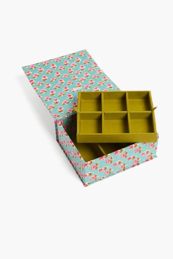 an open box with compartments in it on top of a white surface and floral print paper