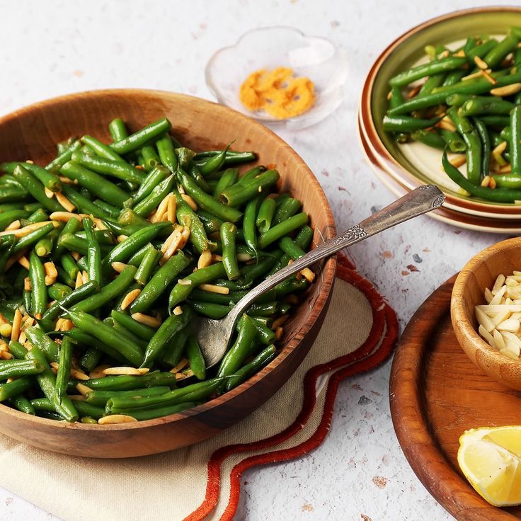 green beans in a wooden bowl with garlic and lemon wedges next to it on a table