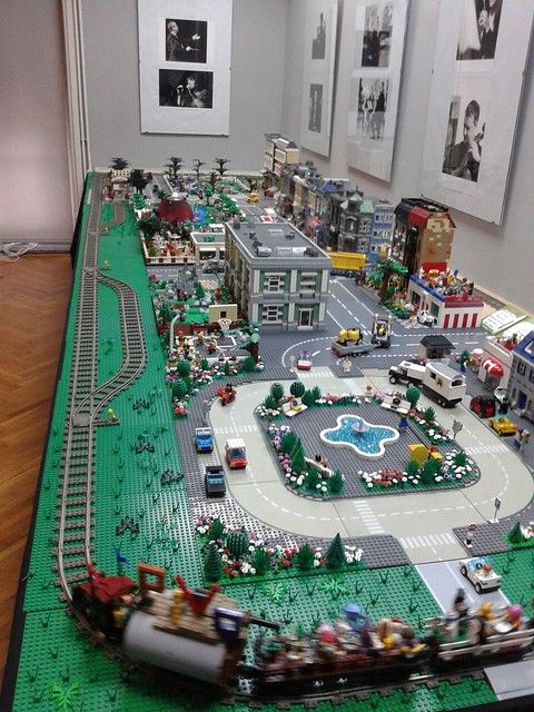 a lego model of a city with cars and people on the street, in front of two framed pictures