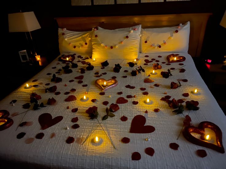 a bed with candles and hearts on it in the night time, surrounded by petals