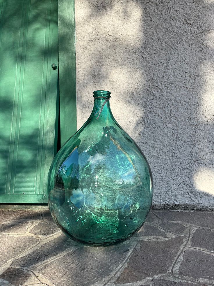 a large green vase sitting on top of a stone floor next to a wall and door