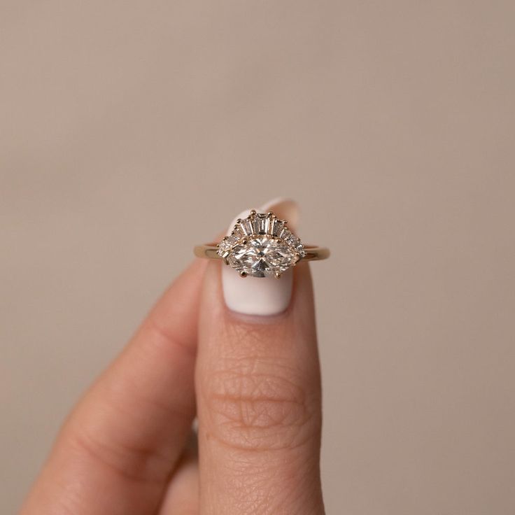 a woman's hand holding an engagement ring with three stones on the top and bottom