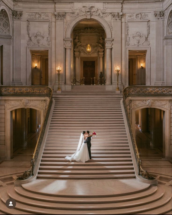 a bride and groom standing on the steps of a grand staircase in an ornate building