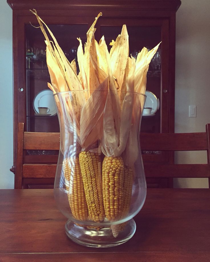 corn on the cob in a glass vase sitting on top of a wooden table