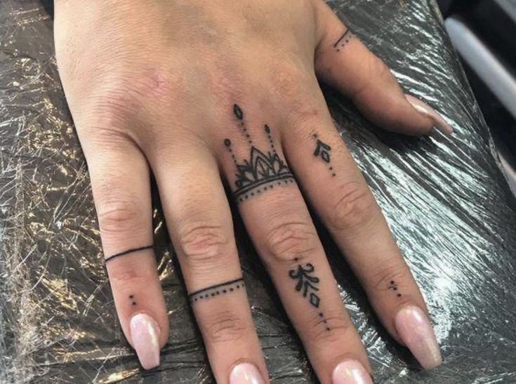 a woman's hand with tattoos on it and a crown tattooed on the middle finger