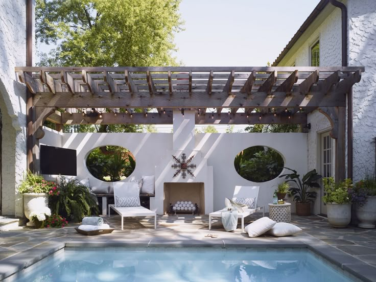 an outdoor living area with a swimming pool and pergolated patio furniture in the foreground