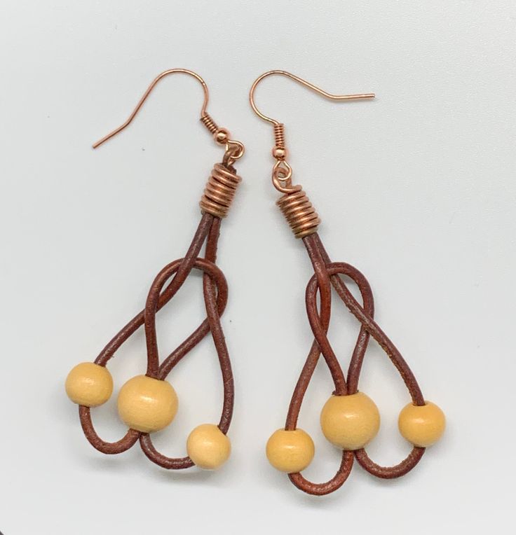 two pairs of earrings with beads hanging from them on a white surface, one is yellow and the other is brown