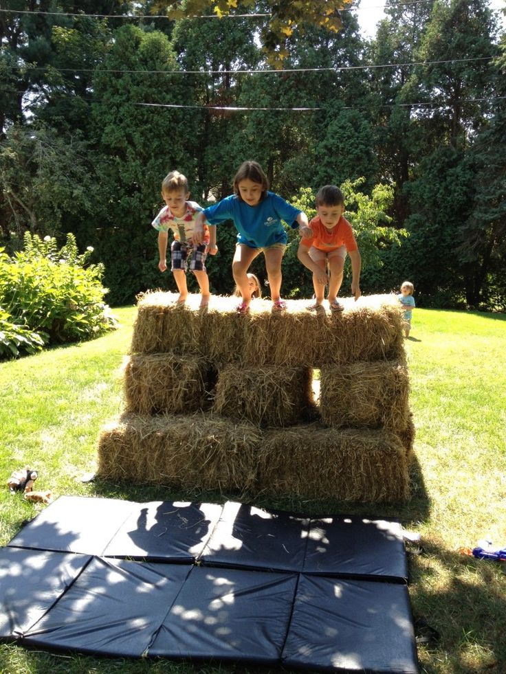 three children are standing on hay bales in the yard and one child is jumping