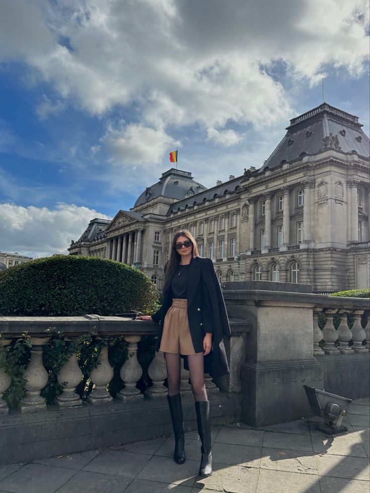 a woman standing in front of a large building on a sunny day with her legs crossed