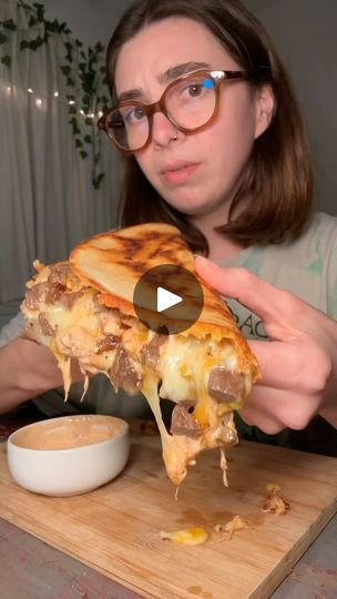 a woman holding up a piece of pizza with cheese and meat on it while sitting at a table