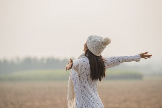 a woman standing in a field with her arms spread out to the side while wearing a hat and scarf