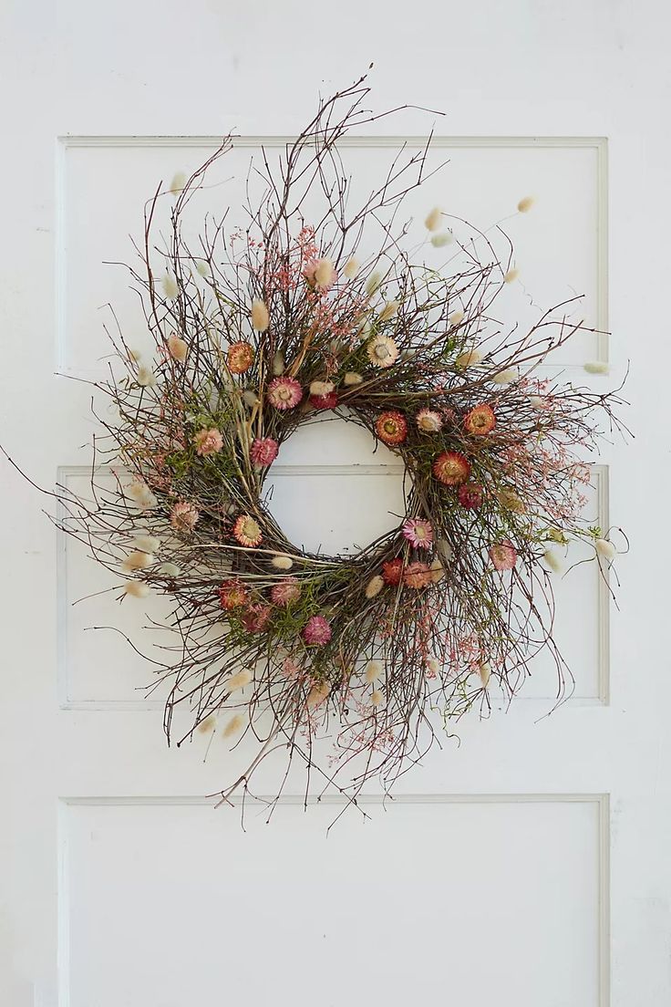 a white door with a wreath hanging on it's side and flowers in the middle