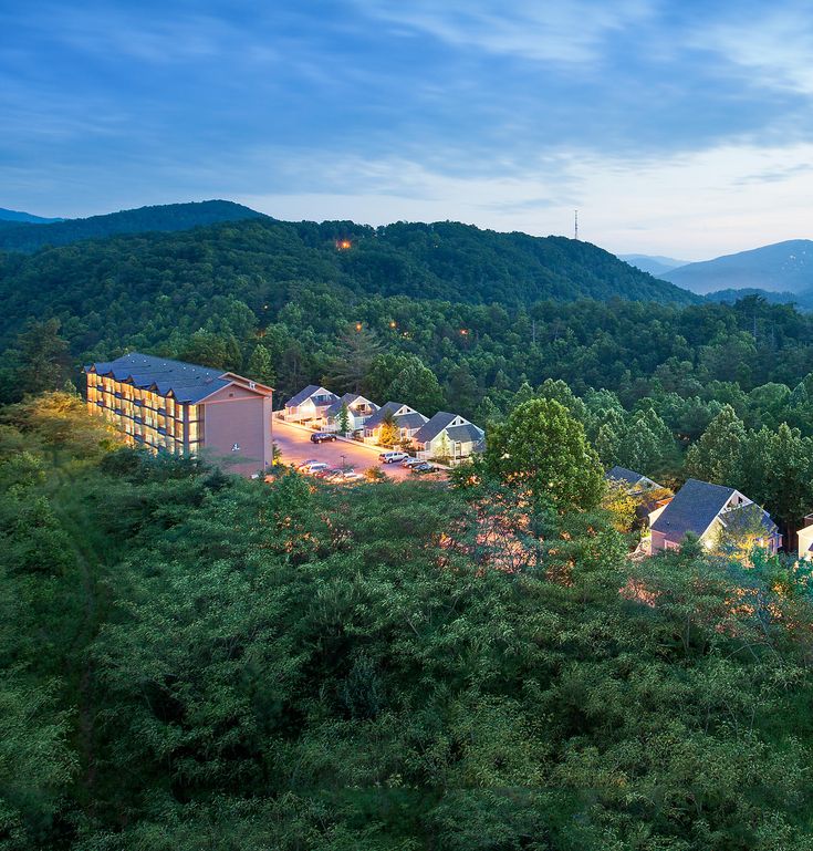 an aerial view of a resort surrounded by trees and mountains at dusk with the lights on