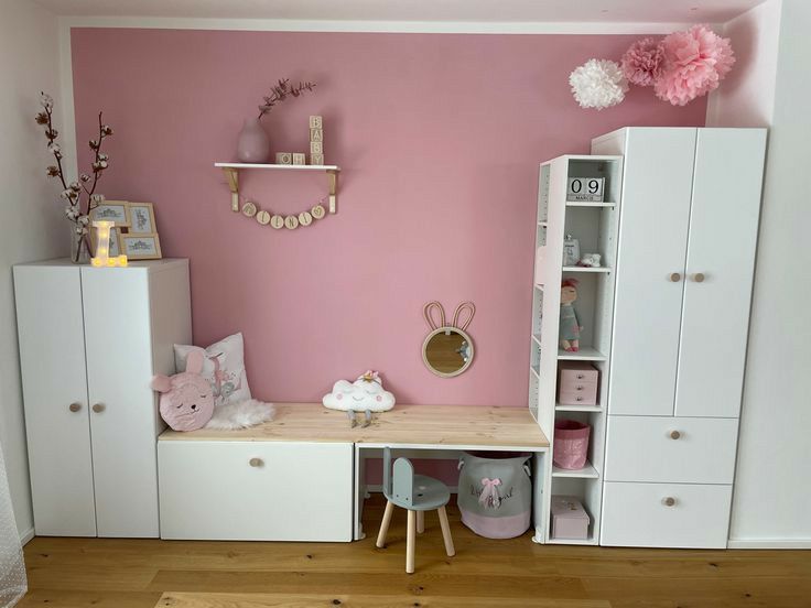 a child's room with pink walls and white furniture