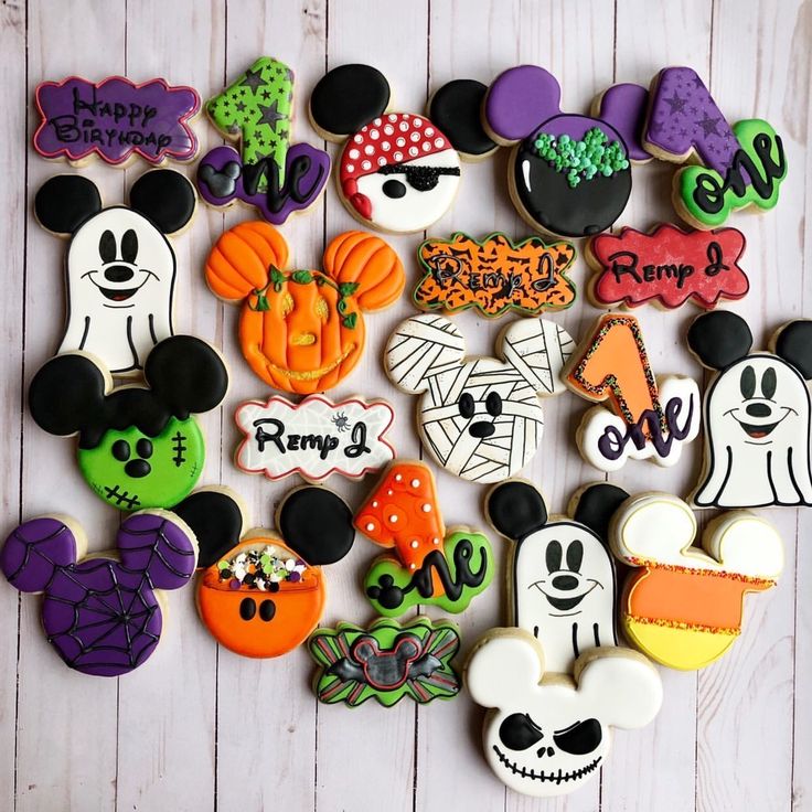 mickey mouse cookies decorated with royal icing and halloween decorations are arranged on a white wooden surface