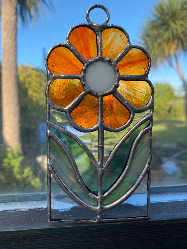 a stained glass sun catcher sitting on top of a window sill with palm trees in the background