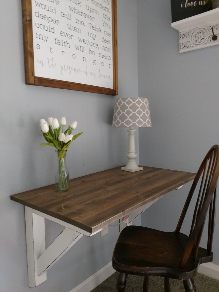 a wooden table with a vase on it next to a chair and framed art above it