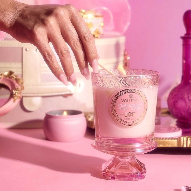 a woman's hand reaching for a candle on a pink table with other items